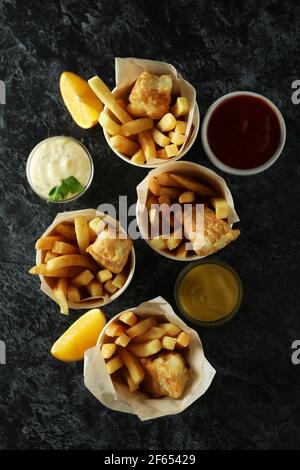 Pappbecher mit frittiertem Fisch und Pommes und Saucen auf schwarzem rauchigen Hintergrund Stockfoto