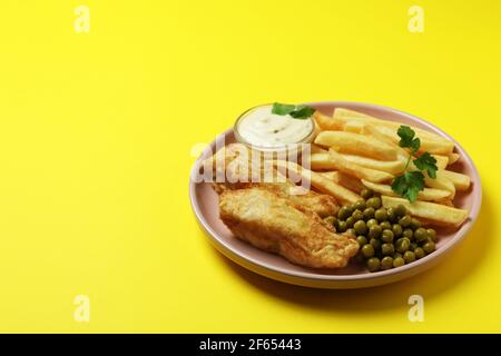 Teller mit gebratenem Fisch und Pommes, Erbse und Sauce auf gelbem Hintergrund Stockfoto