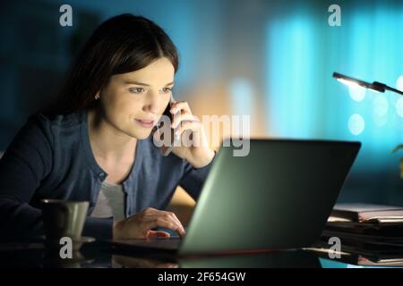 Konzentriert Frau mit Laptop und im Gespräch auf Handy bei Zuhause in der Nacht Stockfoto