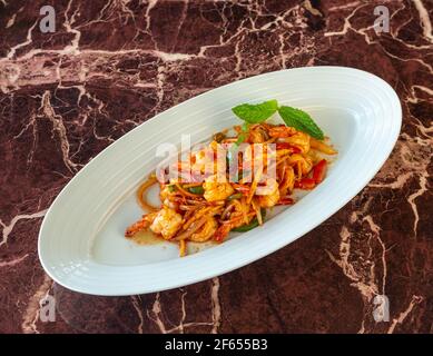 Nudeln mit Gemüse und Garnelen unter Rühren in weißen Keramikschalen anbraten. Schieferhintergrund. Nahaufnahme. Auf Marmorboden. Stockfoto