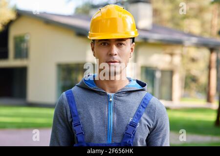 Portrait eines gutaussehenden jungen männlichen Ingenieurs in einem Hut, der die Kamera anschaut, im Freien posiert, während er an der Hüttenkonstruktion arbeitet Stockfoto