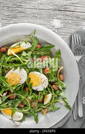 Frischer Löwenzahn-Salat mit Bohnen und Eiern auf Holzhintergrund Stockfoto