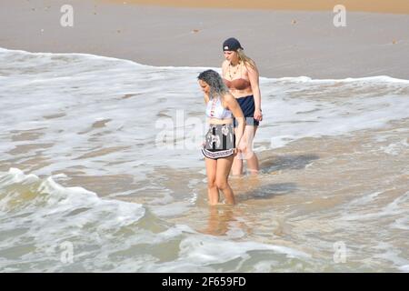 Bournemouth, Dorset, Großbritannien, 30.. März 2021, Wetter. Frühe Frühjahrshitzewelle. Zwei Mädchen paddeln im kalten Meer. Stockfoto