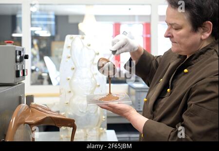 30. März 2021, Brandenburg, Himmelpfort: Sylke Wienold, Leiterin der Himmelpforter Chocolaterie, gießt die Schokolade für die Schokoladenpizza mit einer Pfanne in eine Form. Im kleinen Familienbetrieb im Landkreis Oberhavel gibt es rund 700 Süßwaren; zu Ostern kommen Eier, Kaninchen, Schafe und andere Figuren aus der hellen oder dunklen Schokolade dazu. Der ehemalige Informatiker hat die Zeit der Corona-Sperre genutzt, um einen "Click-and-Collect-Shop" einzurichten. Nach Ostern wird der Laden allerdings vorerst schließen müssen, denn ohne Tourismus und Gastronomie gibt es zu wenig VIS Stockfoto