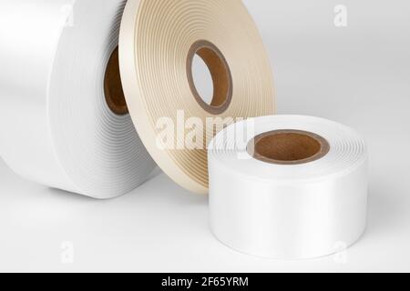 Makrozusammensetzung von drei Coils aus weißen, beigen Satinbändern in verschiedenen Größen für Etiketten oder Branding, isoliert auf weißem, grauem Hintergrund Stockfoto