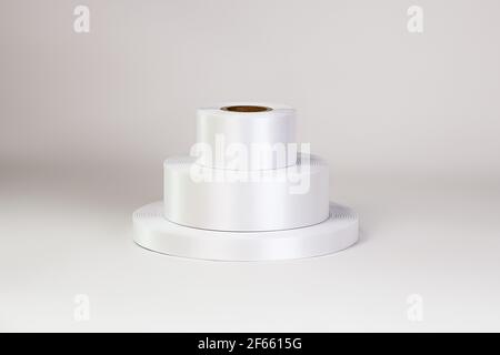 Ein Turm aus drei Spulen von weißen Satinbändern in verschiedenen Größen für Etiketten oder Branding, isoliert auf einem weißen, grauen Hintergrund Stockfoto