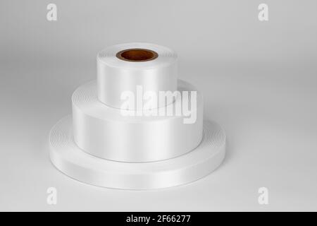 Draufsicht Turm von drei Spulen von weißen Satinbändern in verschiedenen Größen für Etiketten oder Branding, isoliert auf einem weißen, grauen Hintergrund Stockfoto