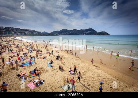 Sonnenanbeter genießen die Osterwoche am Strand La Concha in der Küstenstadt San Sebastian, Donostia, Baskenland. Spanien. Stockfoto