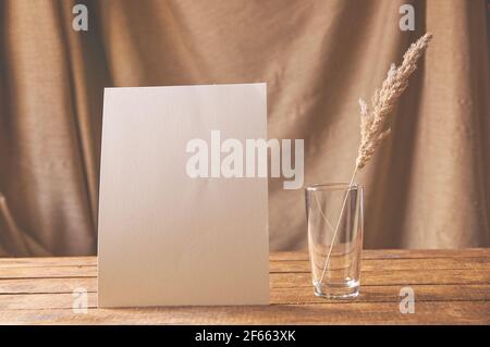Auf dem Tisch ist ein weißes Blatt Papier mit getrockneten Blumen in einem Glas. Für eine Designpräsentation oder ein Portfolio. Stockfoto