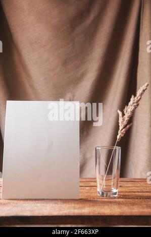 Auf dem Tisch ist ein weißes Blatt Papier mit getrockneten Blumen in einem Glas. Für eine Designpräsentation oder ein Portfolio. Stockfoto
