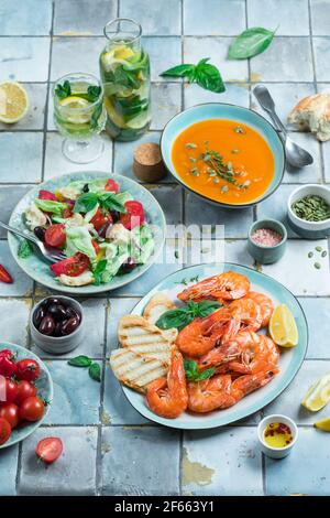 Mediterrane Gerichte am Kacheltisch: Meeresfrüchte-Garnelen, Gemüsesalat, Kürbissuppe, Samen und Fruchtlimonade Stockfoto