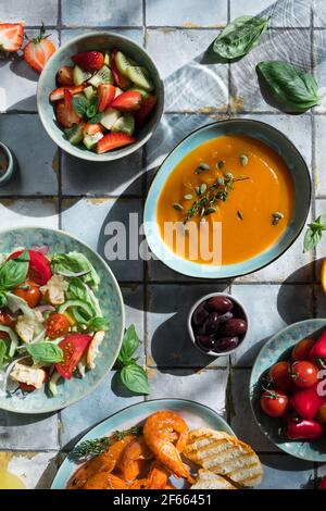 Mediterrane Gerichte am Kacheltisch: Meeresfrüchte-Garnelen, Gemüsesalat, Kürbissuppe, Samen und Fruchtlimonade Stockfoto