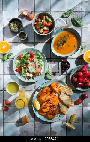 Mediterrane Gerichte am Kacheltisch: Meeresfrüchte-Garnelen, Gemüsesalat, Kürbissuppe, Samen und Fruchtlimonade Stockfoto