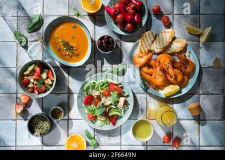 Mediterrane Gerichte am Kacheltisch: Meeresfrüchte-Garnelen, Gemüsesalat, Kürbissuppe, Samen und Fruchtlimonade Stockfoto