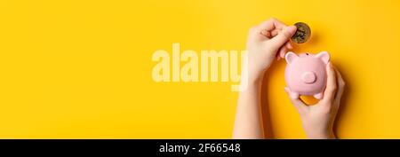Mann Hand hält Bitcoin Münze und Schwein Sparschwein auf gelbem Hintergrund mit Kopierraum. Stockfoto