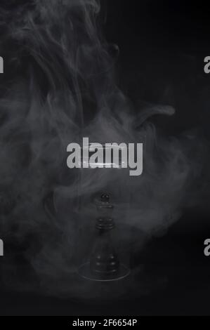 Minimalistische abstrakte Komposition, Glas und Rauch mit einem eingeklemmten Schachstück, das Verschmutzung auf einem dunklen, schwarzen Hintergrund darstellt. Stockfoto