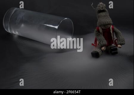 Glas voller Rauch auf dunklem Hintergrund, abstrakte Komposition mit einem Holzspielzeug kleines Mädchen Schlittschuh. Minimalistische abstrakte Komposition, modern. Stockfoto