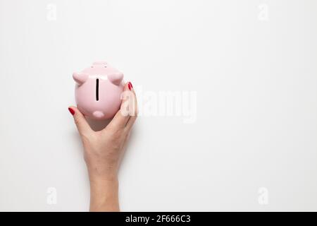 Person Hand hält Schwein Sparschwein mit Geld auf grauem Hintergrund mit Kopierraum. Draufsicht, flach liegend Stockfoto