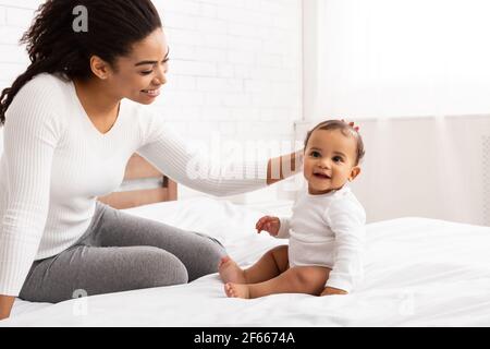 Afrikanisch Amerikanisch Mutter Streichelend Baby Kleinkind Sitzend Auf Bett Innen Stockfoto