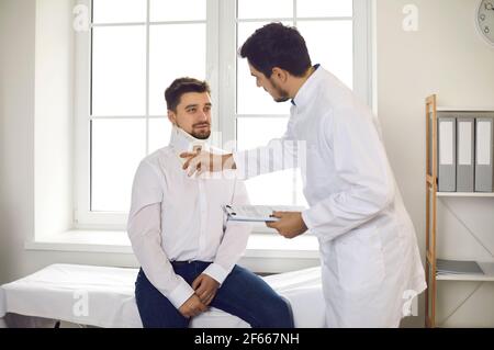 Ein männlicher Physiotherapeut oder Traumatologe untersucht einen männlichen Patienten, der im Halsband sitzt. Stockfoto