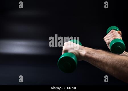Männliche Hände machen Übungen mit kleinen Hanteln auf schwarzem Hintergrund mit Kopierraum. Stockfoto
