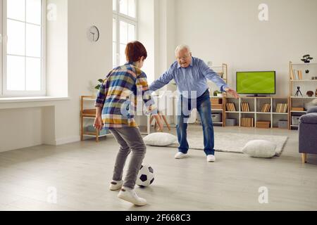 Älterer Großvater spielt Fußball mit Enkel im Wohnzimmer Stockfoto