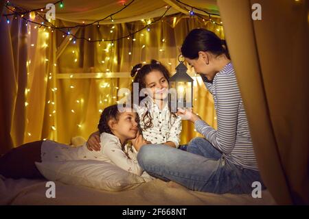 Mutter erzählt zwei kleinen Töchtern magische Geschichte mit Taschenlampe In der Hand Stockfoto