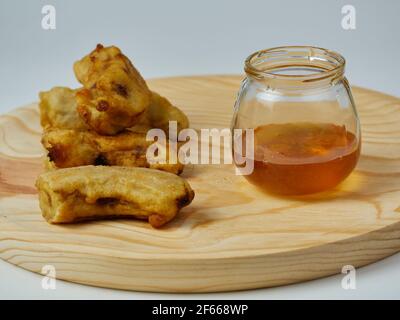 Gebratene Scheiben der reifen Kochbanane und ein Glas davon Honig auf einem runden Holzteller Stockfoto