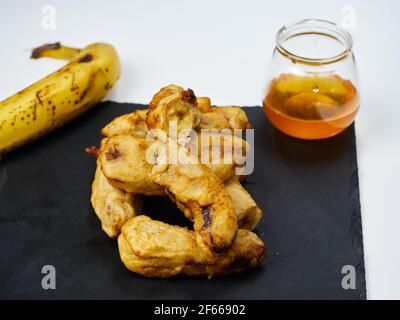 Gebratene Scheiben der reifen Kochbanane mit einer Banane verziert Und Honig auf einem schwarzen Schieferbrett Stockfoto