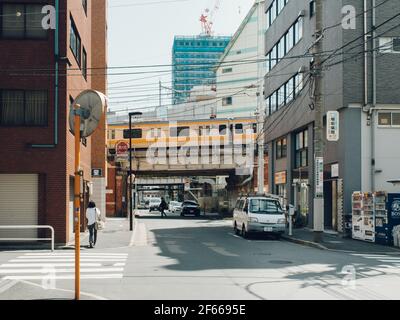 Tokio, Japan - kleine Straße mit dem Zug, der auf der Hochbahn fährt. Ruhige Seitenstraße mit ein paar Leuten und Autos. Stockfoto