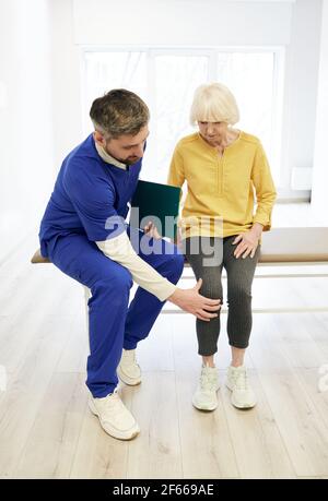 Physiotherapeut, der das Knie des Patienten untersucht. Eine ältere Patientin mit Knieverletzung besucht ihren Physiotherapeuten Stockfoto