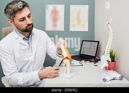 Reifer Arzt mit einem Knie-Gelenk anatomischen Modell zur Analyse der menschlichen Knieprobleme Bereiche und Behandlung Stockfoto