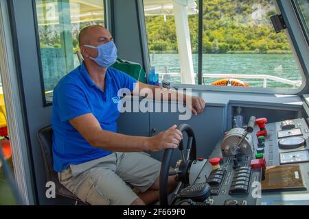 SKIPPER MIT MASKE FÄHRT ELEKTROBOOT AUF DEM FLUSS KRKA Stockfoto