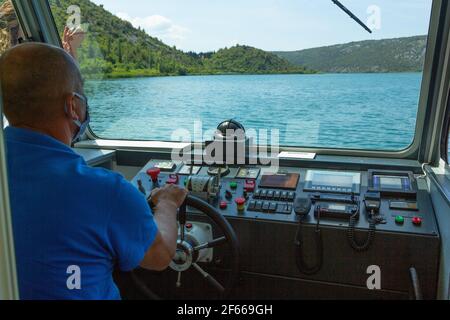 SKIPPER MIT MASKE FÄHRT ELEKTROBOOT AUF DEM FLUSS KRKA Stockfoto