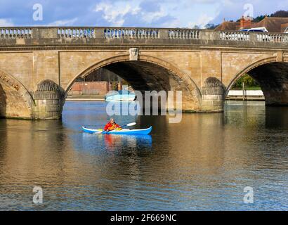 Kanute, die in Henley-on-Thames, Oxfordshire, England, durch die alte Henley Bridge, die über die Themse führt, gepaddelt war Stockfoto