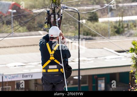 Ein Telefoningenieur, der auf einer Leiter steht, die oben an einem Telegrafenmast arbeitet. Es ist ein sonniger Tag und hinter ihm treten Dächer in die Ferne zurück. Stockfoto