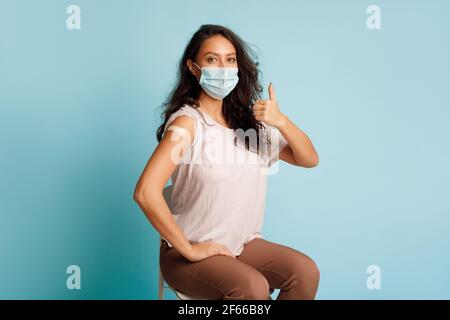 Geimpfte Frau Gestikuliert Thumbs-Up Nach Coronavirus-Impfung Auf Blauem Hintergrund Stockfoto