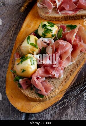 Snack-Vorspeise mit Vollkornbrot, rohem Schinken und geräucherten Provola-Kugeln in Öl Stockfoto