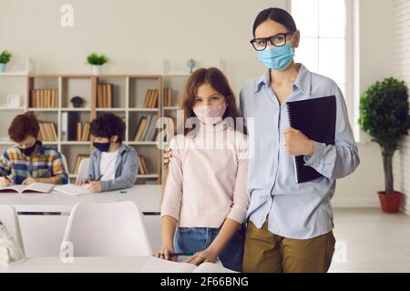 Porträt von Lehrer und Schüler in medizinischen Gesichtsmasken Im Klassenzimmer stehen Stockfoto