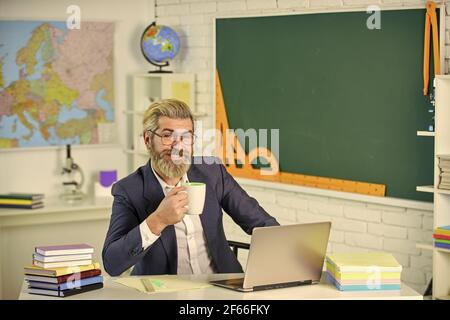 Kaffee im Kopf. Bärtiger Mann trinkt Kaffee im Lehrerzimmer. Senior Professor halten Kaffeetasse. Kaffeepause genießen. Schulpausenzeit. Computer Stockfoto