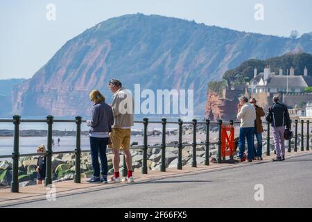 Sidmouth, Devon, Großbritannien. März 2021, 30th. Wetter in Großbritannien: Die Menschen strömen in den Badeort Sidmouth, Devon, um die herrliche Sonne zu genießen, während die Südküste vor dem Osterfeiertagswochenende in einer Mini-März-Hitzewelle sonnt. Man sah die Leute an diesem Nachmittag entlang der hübschen Esplanade spazieren gehen und die heiße Sonne im hübschen Regency Resort genießen. Kredit: Celia McMahon/Alamy Live Nachrichten Stockfoto
