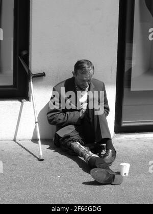 Behinderter obdachloser Mann mit amputierten Bein auf der Stadtstraße, der Geld von vorbeifahrenden Touristen auf der Stadtstraße in Frankreich verlangt, der rau schläft. Stockfoto
