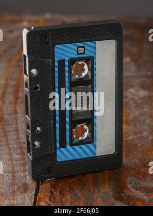 Die Audiocassette in einem klassischen schwarzen Gehäuse steht randbeet vor einem braunen Holzhintergrund. Draufsicht von der Seite. Nahaufnahme Stockfoto