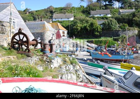Alte Winde und Fischerboote mit reetgedeckten Hütten auf dem Hügel hinter Cadgwith Harbour Cornwall, Großbritannien Stockfoto