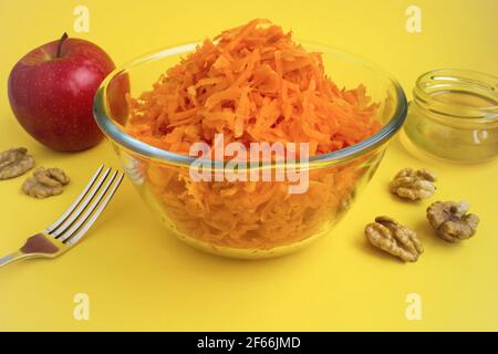 Geriebene Karotte in die Glasschüssel und Zutaten für den Salat Auf dem gelben Hintergrund Stockfoto