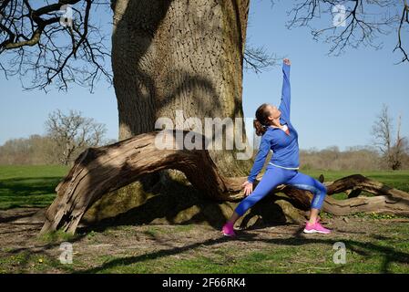 Eine Frau mittleren Alters, die Übung nimmt. Yoga im Freien. Pose des Sonnenkriegers. Stockfoto