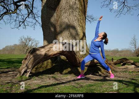 Eine Frau mittleren Alters, die Übung nimmt. Yoga im Freien. Pose des Sonnenkriegers. Stockfoto