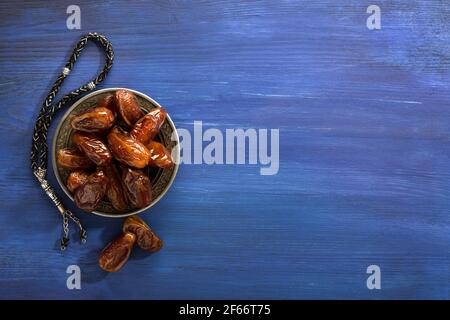 Silberner Teller mit Datteln und tasbih (Misbaha) auf altem dunkelblauen Holztisch. Ramadan Hintergrund. Flach liegend. Selektiver Fokus. Stockfoto