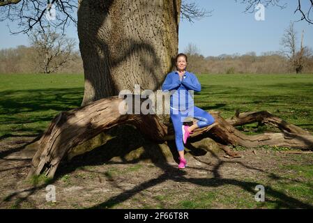 Eine Frau mittleren Alters, die Übung nimmt. Baum Pose in Yoga unter und Eiche. Stockfoto
