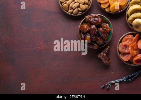 Kleine Teller mit getrockneten Früchten (Dattelpalmen, getrocknete Aprikosen, Feigen) und Nüssen (Mandeln) für Iftar im Ramadan auf dem dunkelrot-braunen Holztisch. Stockfoto